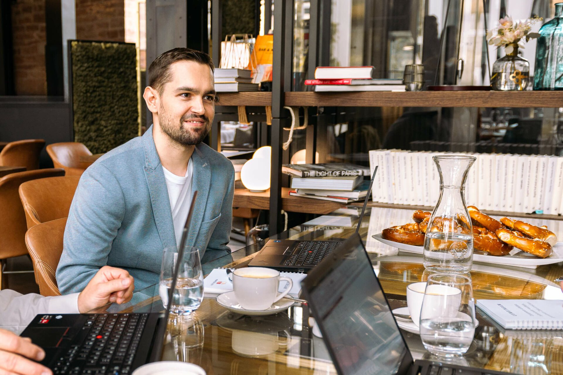 Besprechungsszenario, gedeckter Tisch, ein Mitarbeiter im Fokus, freundlich lächelnder junger Mann